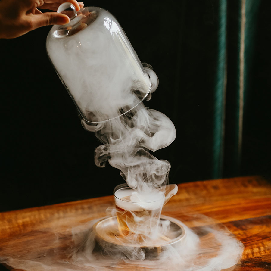 Smoke rising from a tableside presentation of a smoked cocktail.